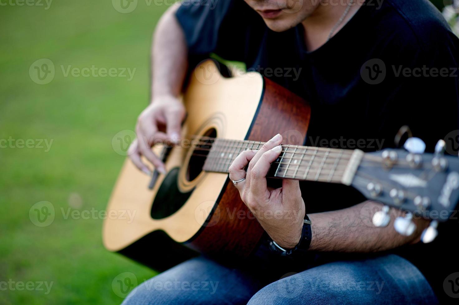 Bild eines Gitarristen, eines jungen Mannes, der Gitarre spielt, während er in einem natürlichen Garten sitzt, Musikkonzept foto