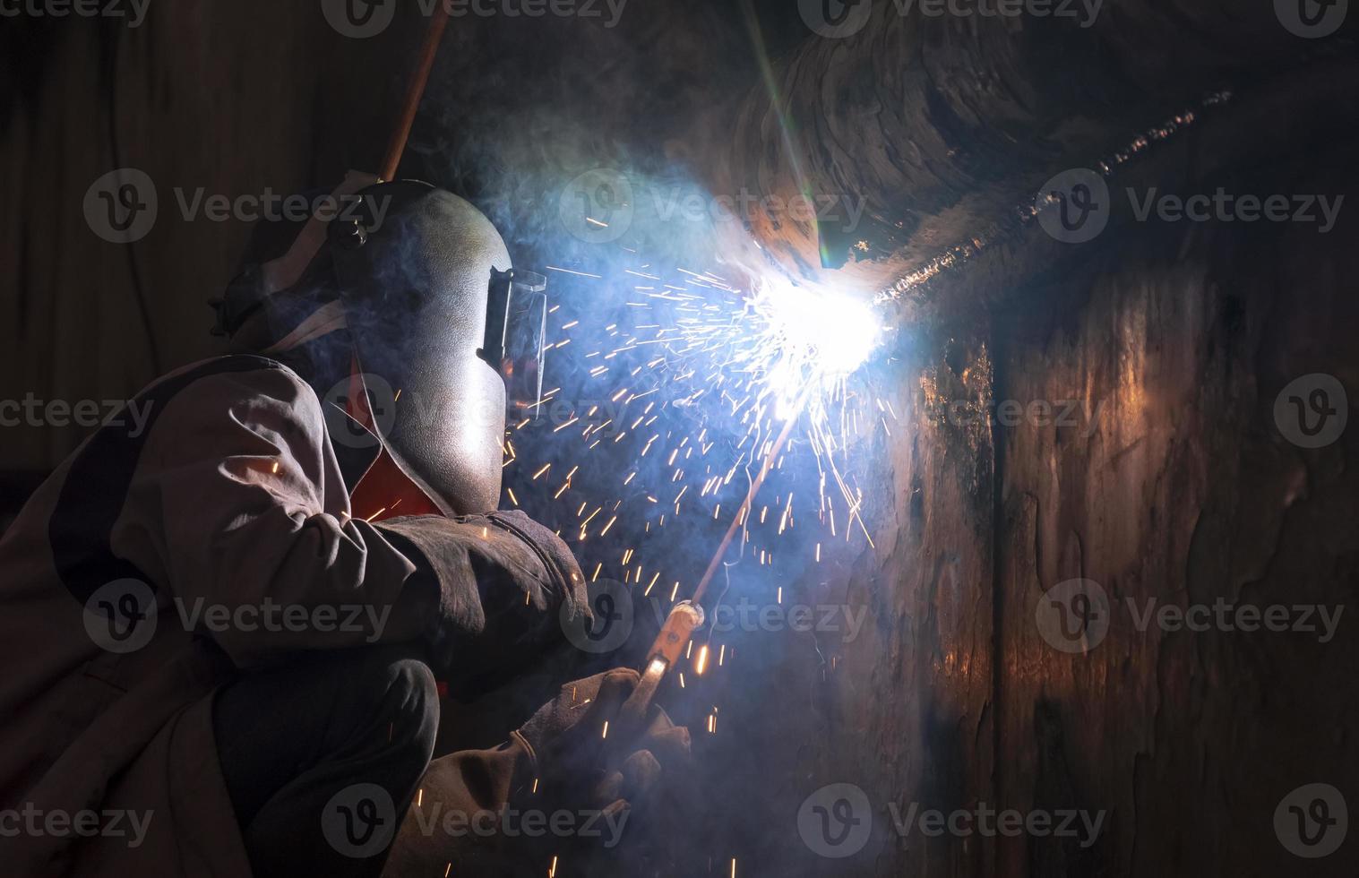 Schweißer in Schweißmaske schweißt Metallwand des alten Fischereifahrzeugs auf der Werft im dunklen Tonstil foto