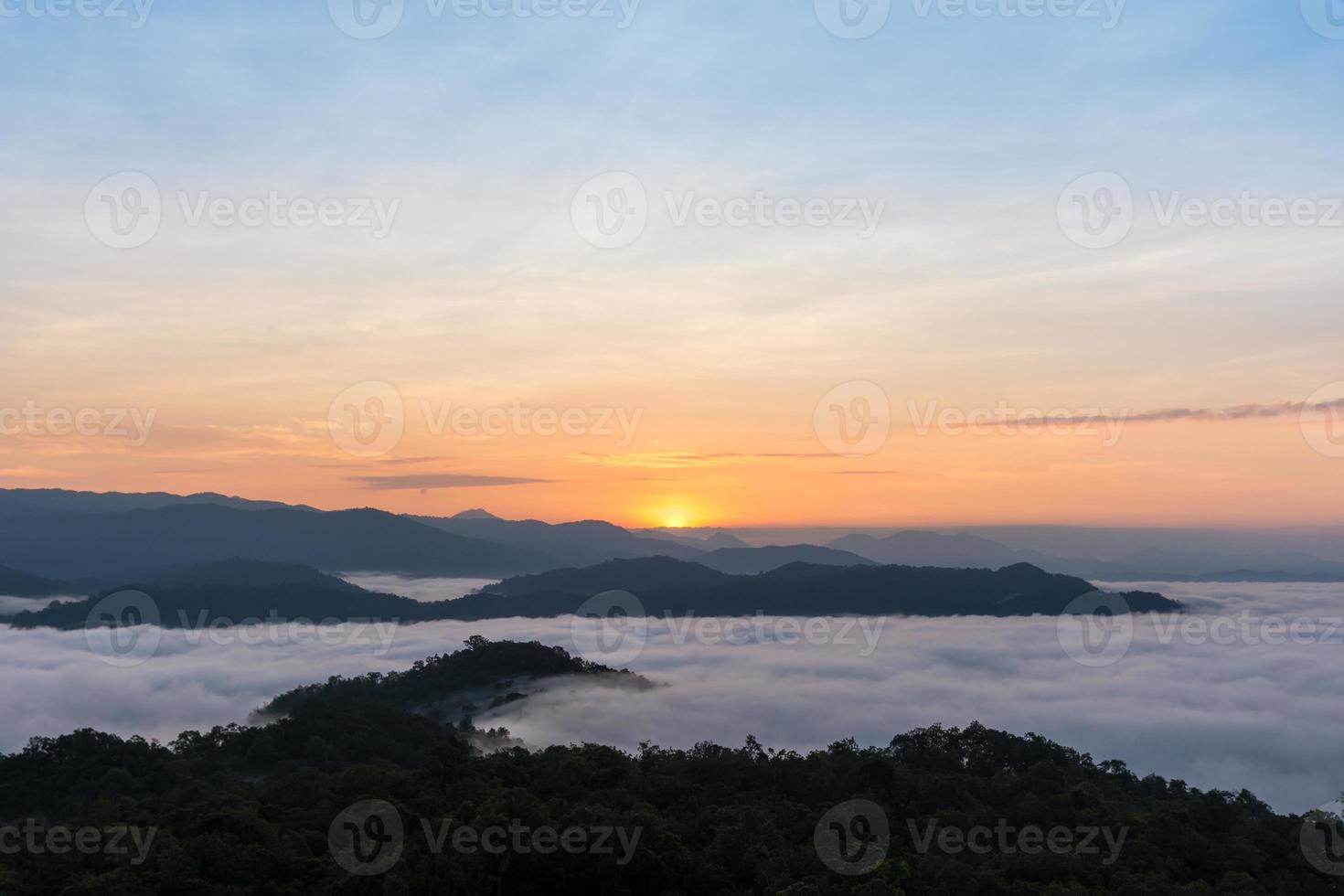 Sonnenaufgang über großen Bergen und Nebel über Wald im Winter foto