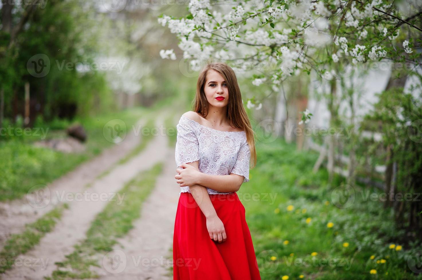 Porträt eines schönen Mädchens mit roten Lippen im Frühlingsblütengarten, trägt ein rotes Kleid und eine weiße Bluse. foto