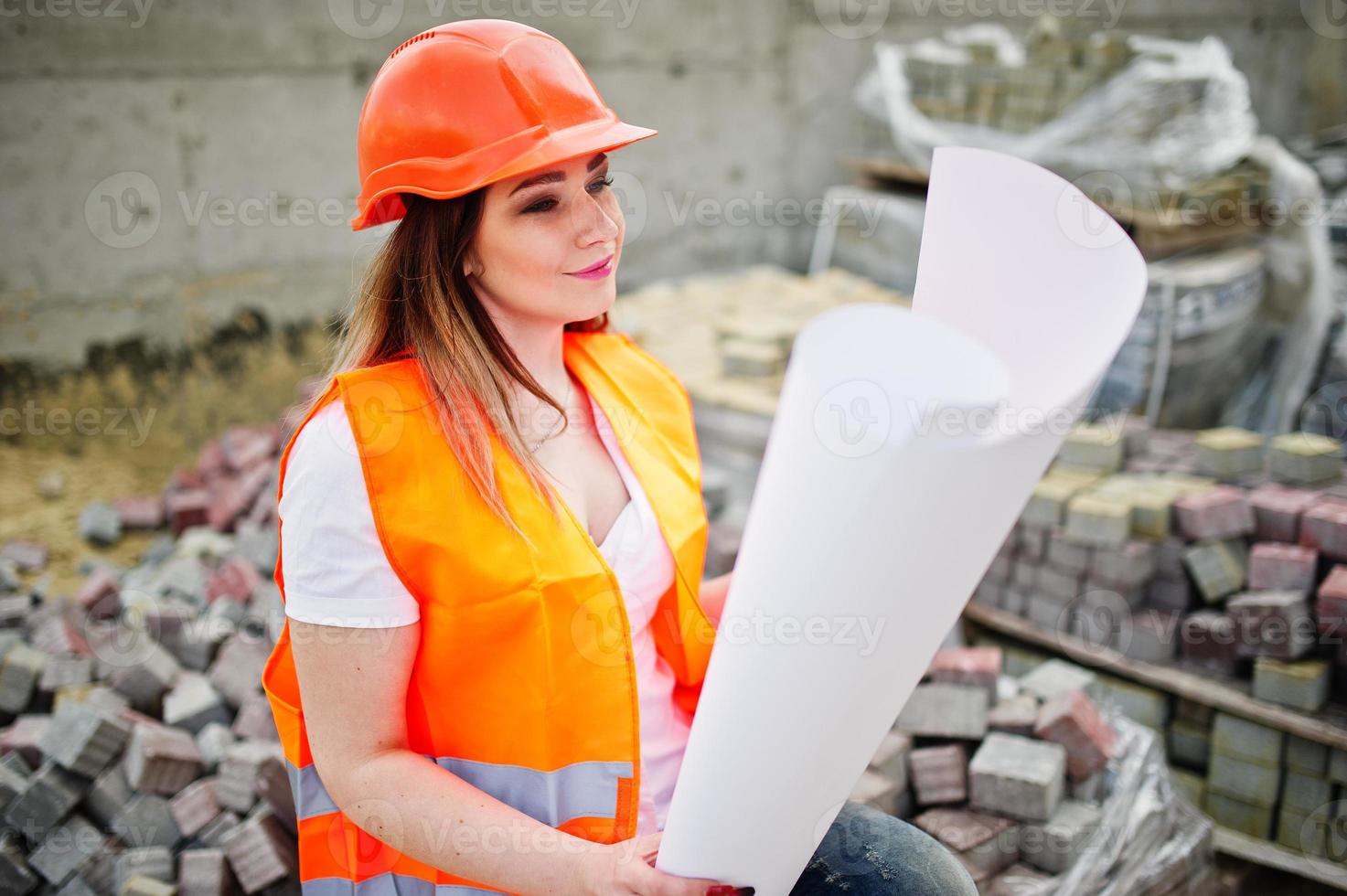 ingenieurbaumeisterin in uniformweste und orangefarbenem schutzhelm halten geschäftsplanpapier, das auf bürgersteig sitzt. foto