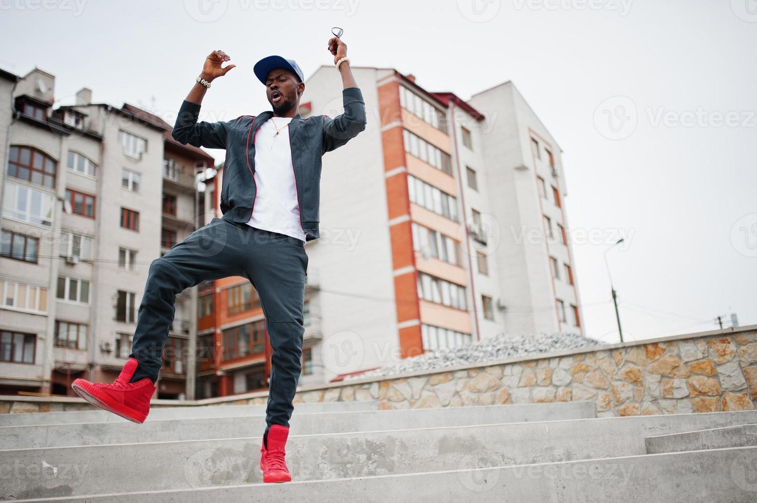 Porträt eines springenden, stilvollen afroamerikanischen Mannes auf Sportbekleidung, Mütze und Brille. schwarze Männer Emotion Model Street Fashion. foto