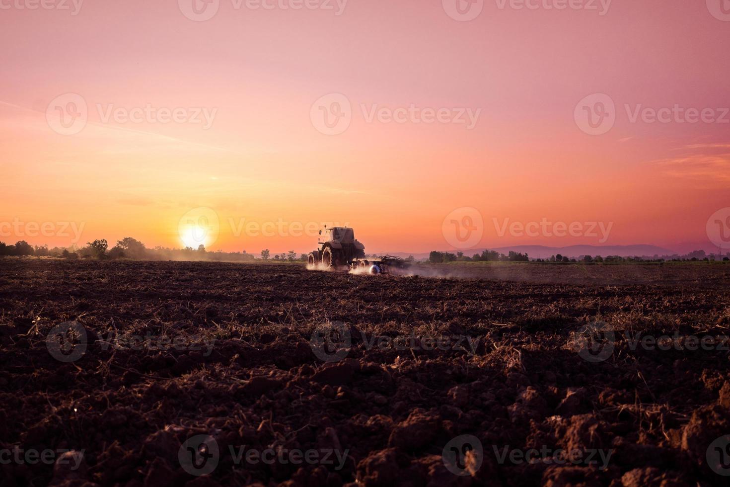 Maschine, die bei Sonnenuntergang auf Ackerland arbeitet foto