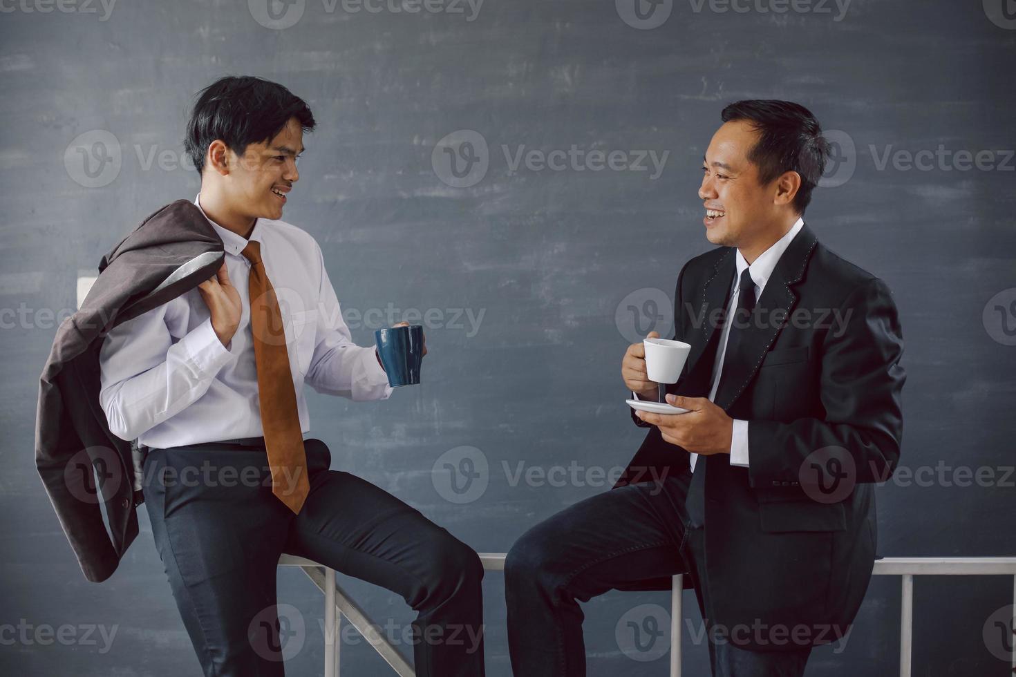 Zwei asiatische Geschäftsleute unterhalten sich, während sie in einer Pause Kaffee halten foto