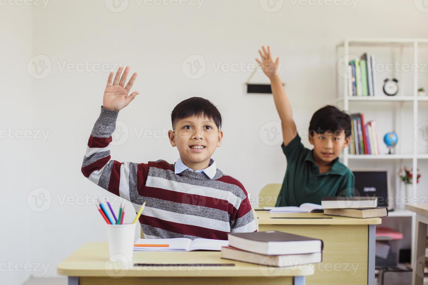 kluge asiatische grundschüler, die ihre hand in der klasse heben, um die lehrerfrage zu beantworten foto