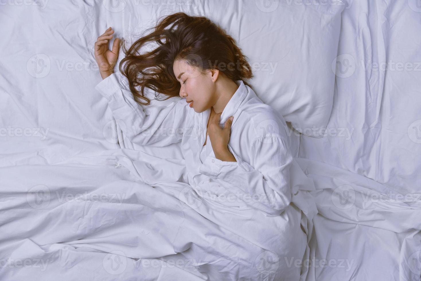 junge Frau, die im Bett schläft. Blick von oben auf die junge Frau, die sich hinlegt und gut im Bett schläft. Schlafen entspannen, junge lächelnde hübsche Dame liegt im Bett. foto