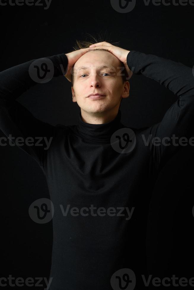 Porträt eines entschlossenen, gutaussehenden Mannes mit schwarzem Hemd, schwarzem Hintergrund. foto