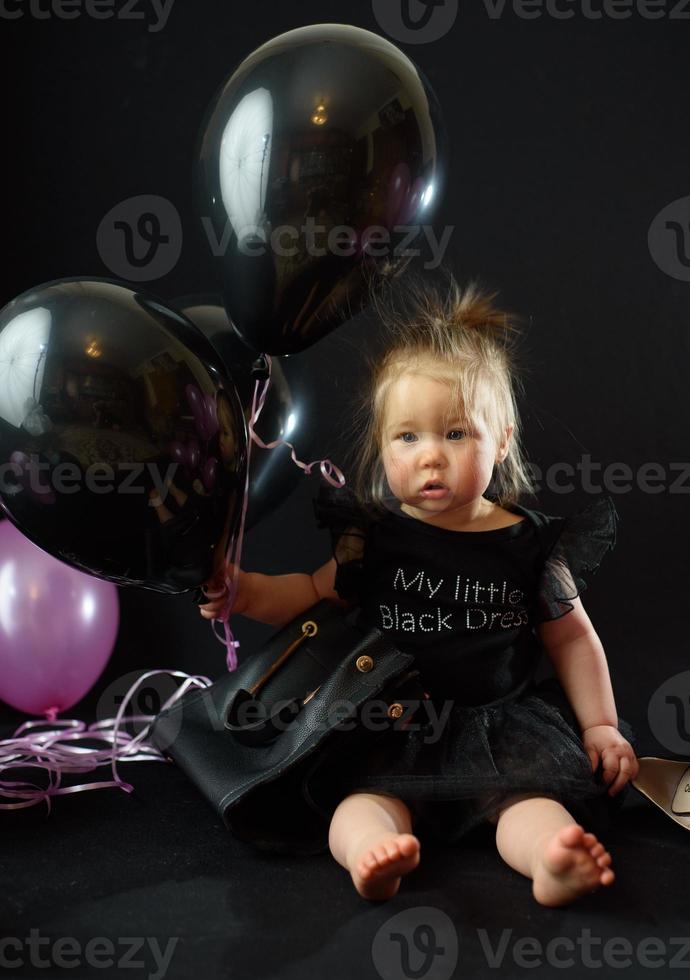 Geburtstagsfeiertag des ersten Jahres des Babymädchens. Ballons und Urlaub drinnen. Geburtstag des Kindes. kleines hübsches Mädchen in ihrem ersten schwarzen Kleid foto