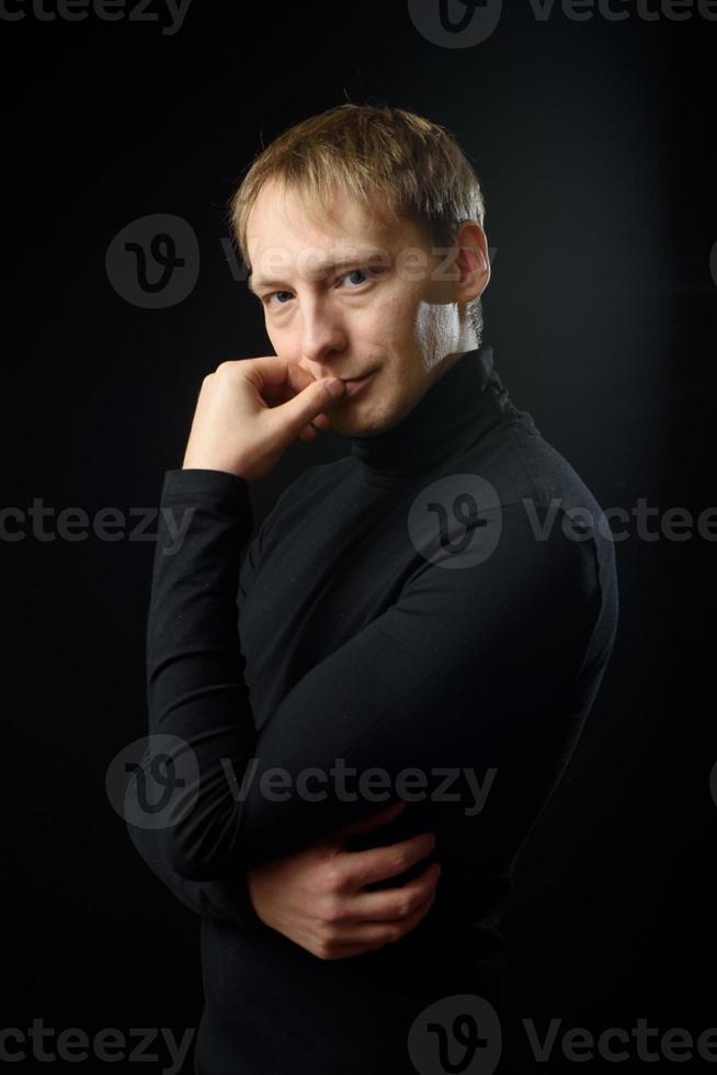 Porträt eines entschlossenen, gutaussehenden Mannes mit schwarzem Hemd, schwarzem Hintergrund. foto