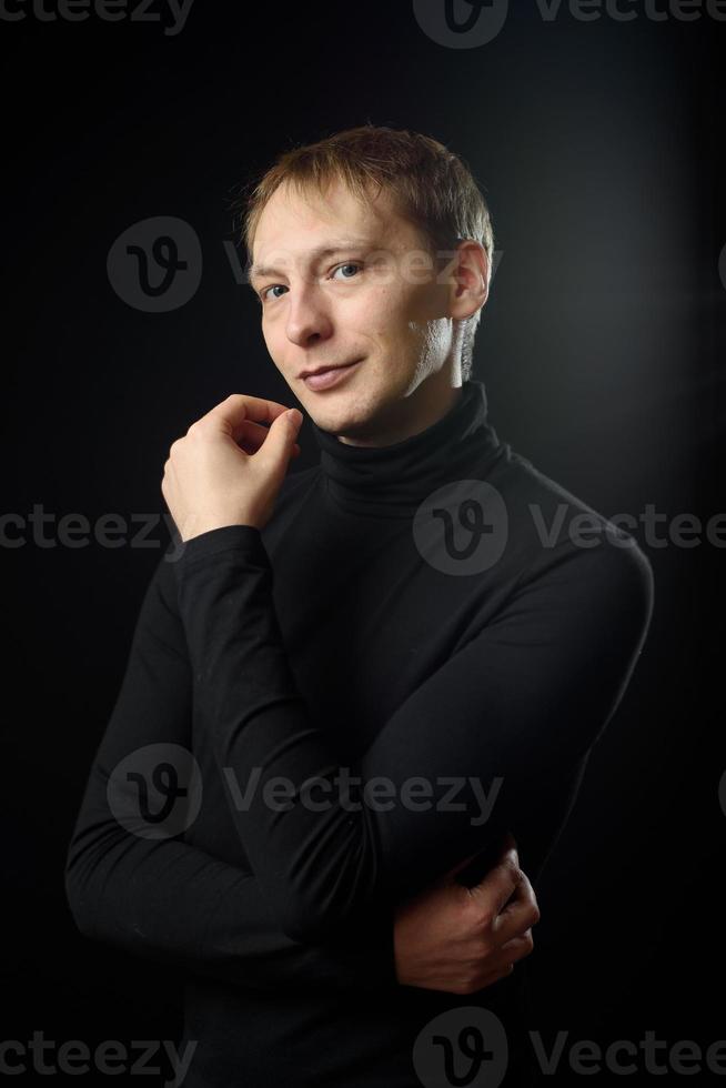 Porträt eines entschlossenen, gutaussehenden Mannes mit schwarzem Hemd, schwarzem Hintergrund. foto