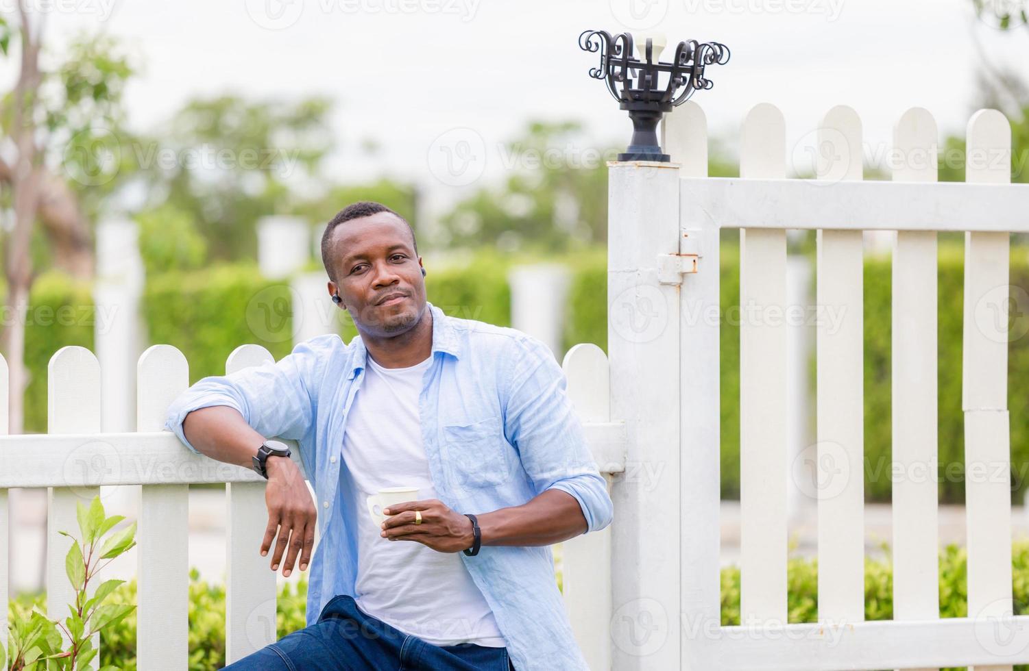 Fröhlicher afrikanisch-amerikanischer Mann, der Papierglas hält, lächelt im Freien und blickt in die Kamera foto