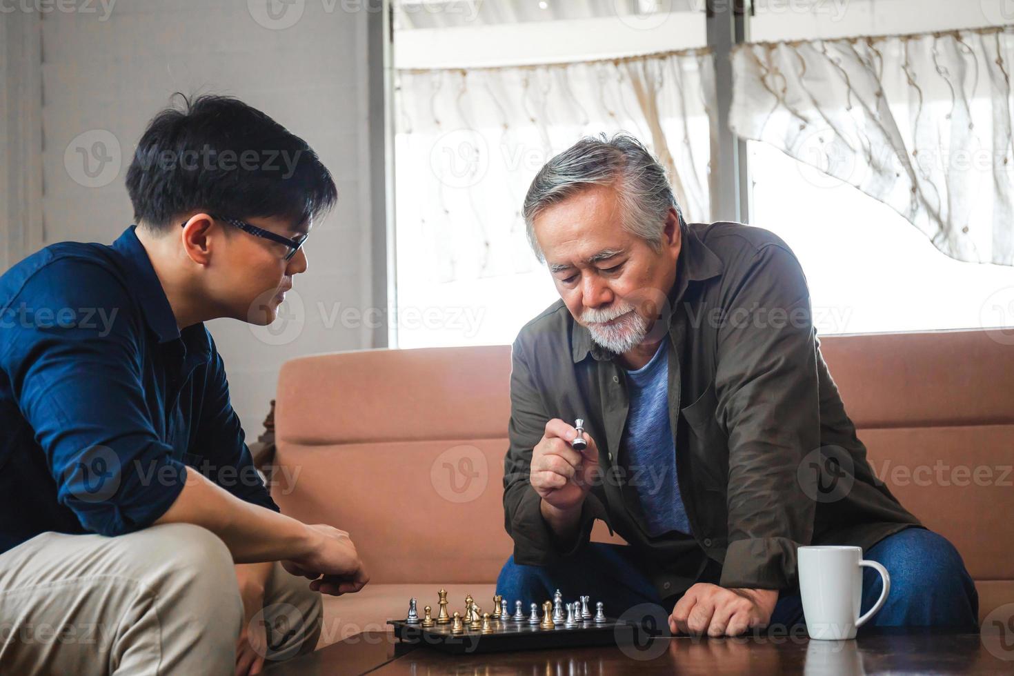 älterer asiatischer vater und sohn mittleren alters, die schachspiel im wohnzimmer spielen, glück asiatische familienkonzepte foto