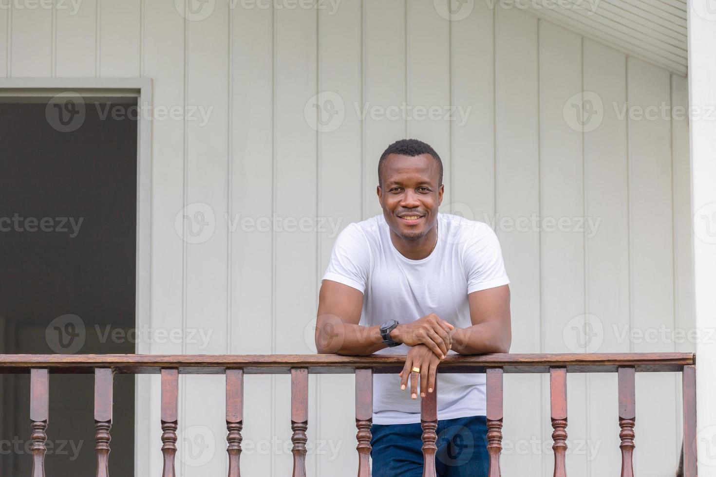 Fröhlicher afroamerikanischer Mann auf Holzbalkon und Blick in die Kamera foto