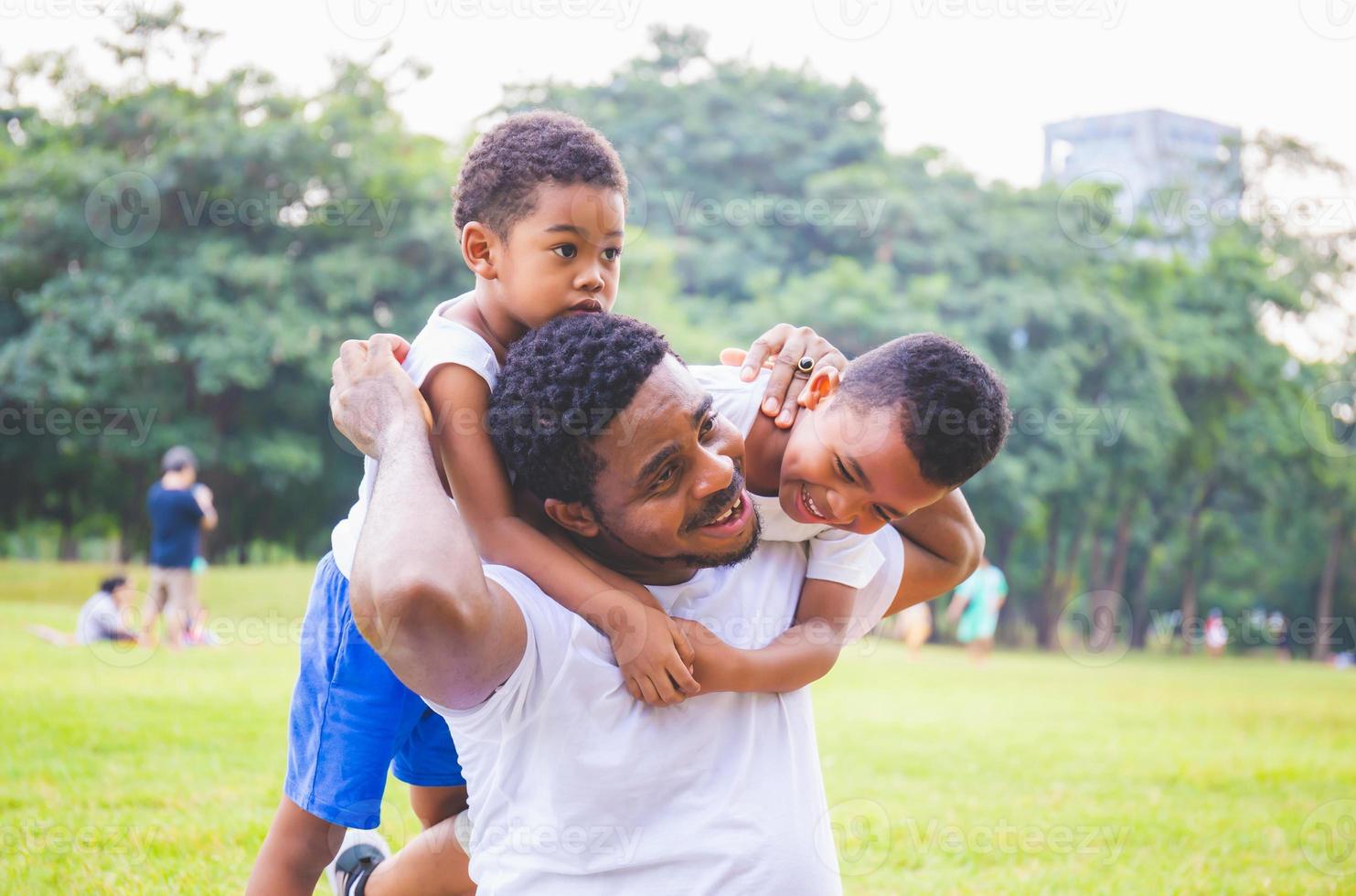 fröhlicher afroamerikanischer vater und zwei söhne spielen im park, glücksfamilienkonzepte, eltern und kinder spielen im park foto