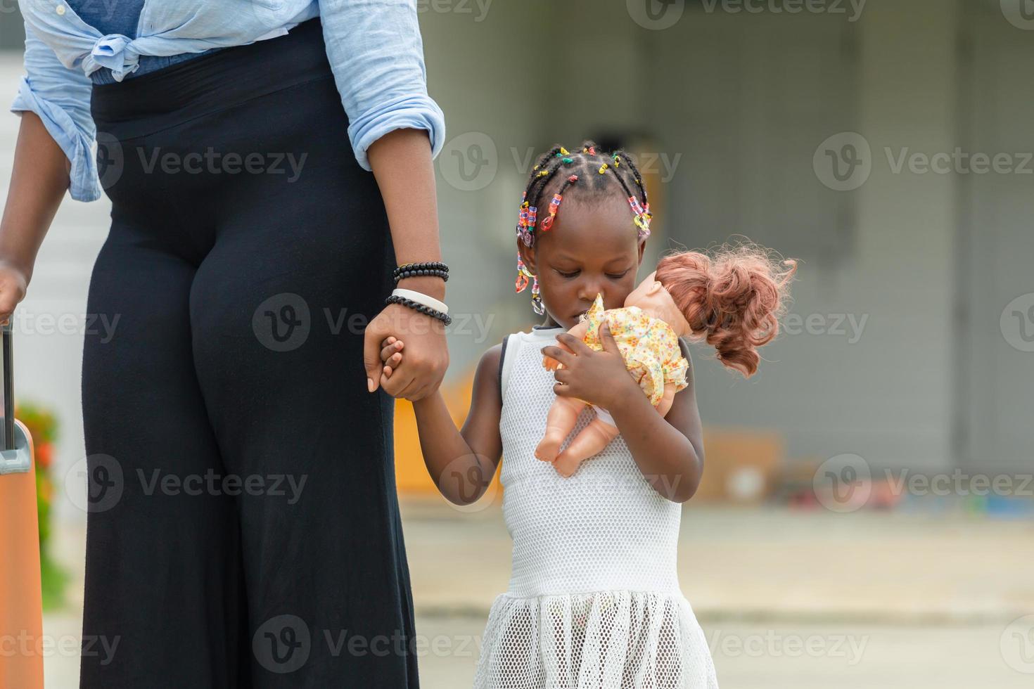 afroamerikanische mutter, die hand ihrer tochter hält, leider kleines mädchen, das ihre puppe hält und umarmt foto