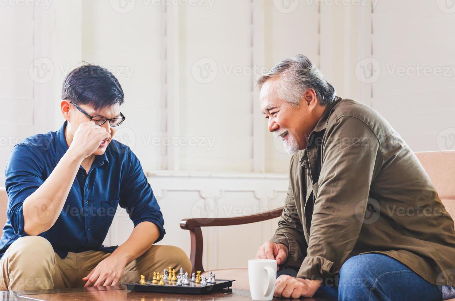 sohn mittleren alters und älterer asiatischer vater spielen schachspiel im wohnzimmer, glück asiatische familienkonzepte foto