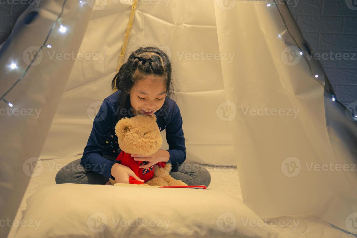 kleines mädchen, das ein buch im zelt liest, glückliches kind, das zu hause spielt, lustiges nettes kind, das spaß im kinderzimmer hat. foto