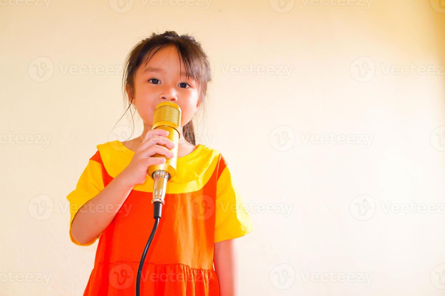 schönes baby trägt ein gelb-orangees outfit, gokowa-outfit oder mugunghwa, und hält goldenes mikrofon, das musik singt. Modekleid für Mädchen und Teenager. foto