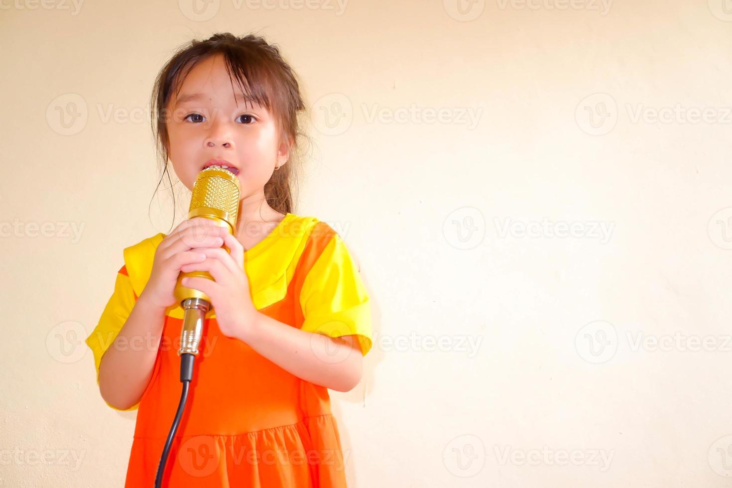 schönes baby trägt ein gelb-orangees outfit, gokowa-outfit oder mugunghwa, und hält goldenes mikrofon, das musik singt. Modekleid für Mädchen und Teenager. foto