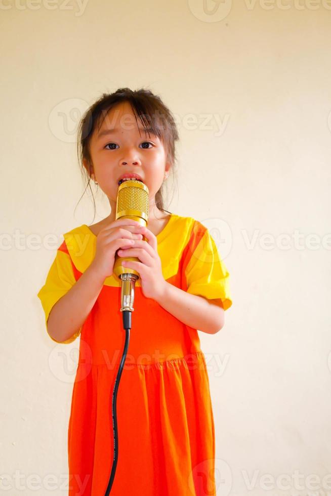 schönes baby trägt ein gelb-orangees outfit, gokowa-outfit oder mugunghwa, und hält goldenes mikrofon, das musik singt. Modekleid für Mädchen und Teenager. foto