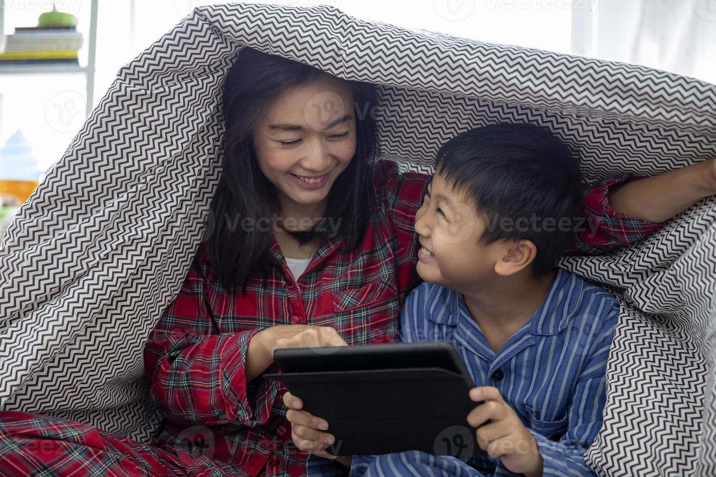 eine glückliche asiatische familienmutter und ein sohn machen zusammen aktivitäten im wohnzimmer, spielen ein spiel auf einem digitalen tablet und lächeln glücklich, während sie zeit zusammen zu hause verbringen foto