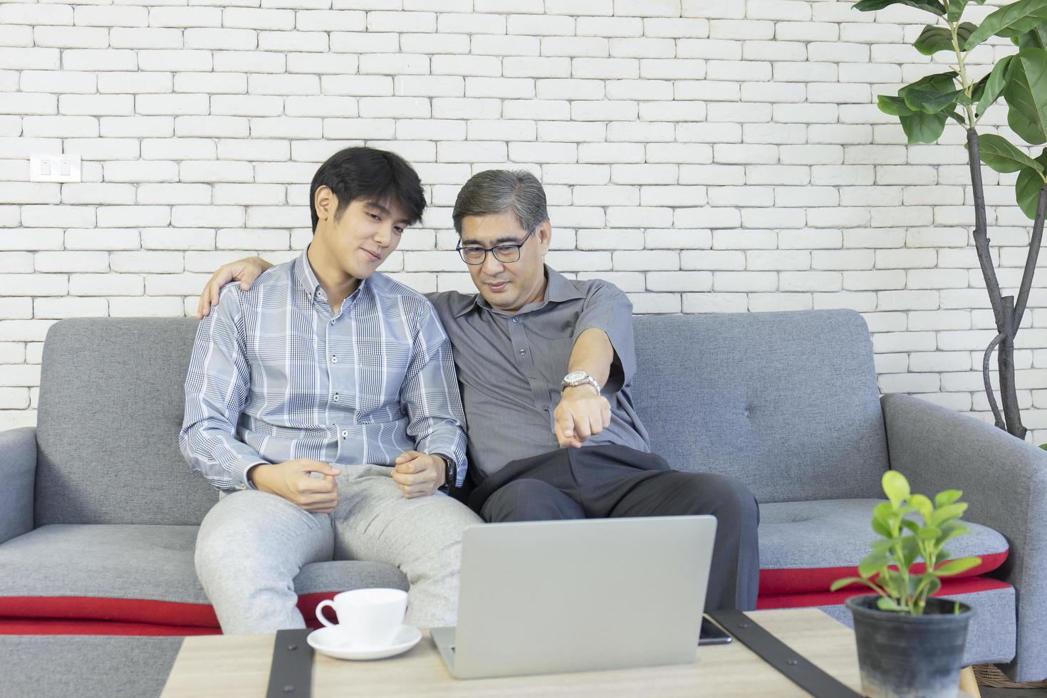 Ein Vater und ein asiatischer Sohn sitzen auf dem Sofa und unterhalten sich über einen Videoanruf auf einem Laptop. foto