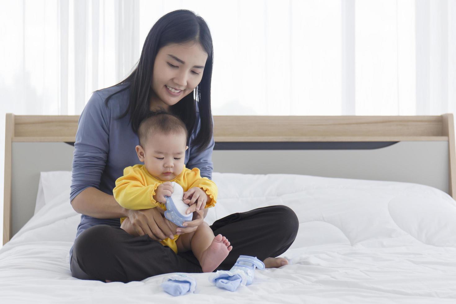 Eine asiatische Mutter legt ihr Baby auf den Schoß und ist dabei, die Schuhe ihres Babys anzuziehen. foto