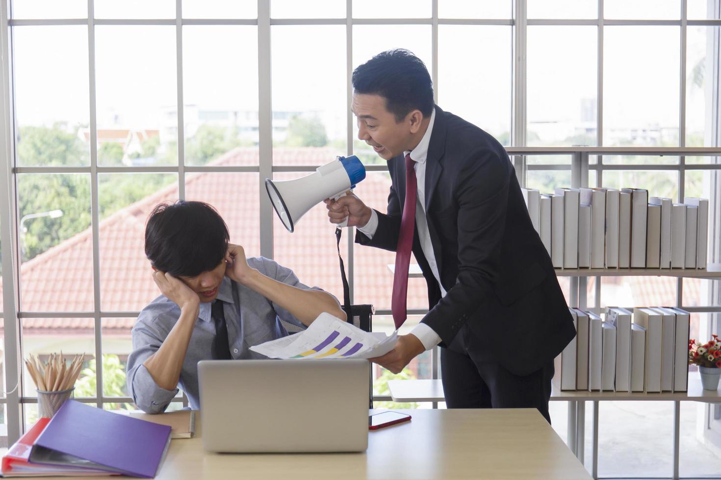 Ein wütender asiatischer Manager, der seinem Untergebenen über einen Lautsprecher ins Ohr schreit, um Dokumente zu holen. foto