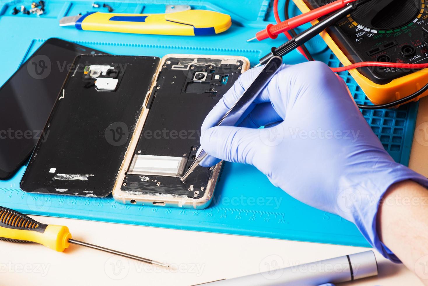 Handwerker in Gummihandschuhen reparieren oder warten ein Mobiltelefon auf einer speziellen Gummimatte zur Reparatur. Ansicht von innen foto