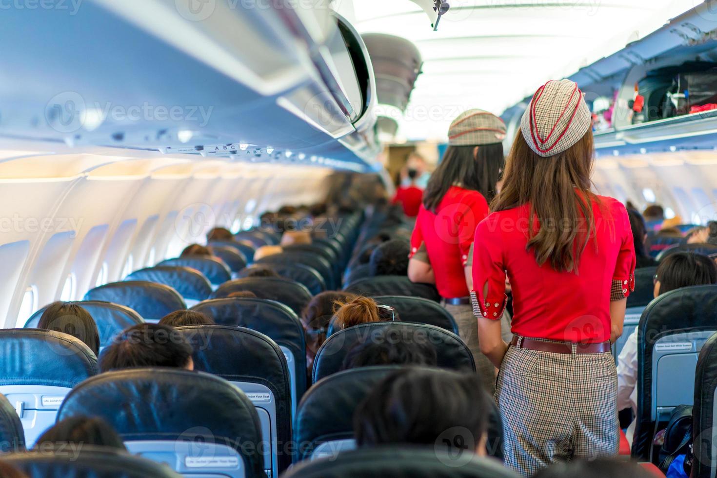 Stewardess in roter Uniform bedient und kontrolliert alles rund um den Passagiersitz foto
