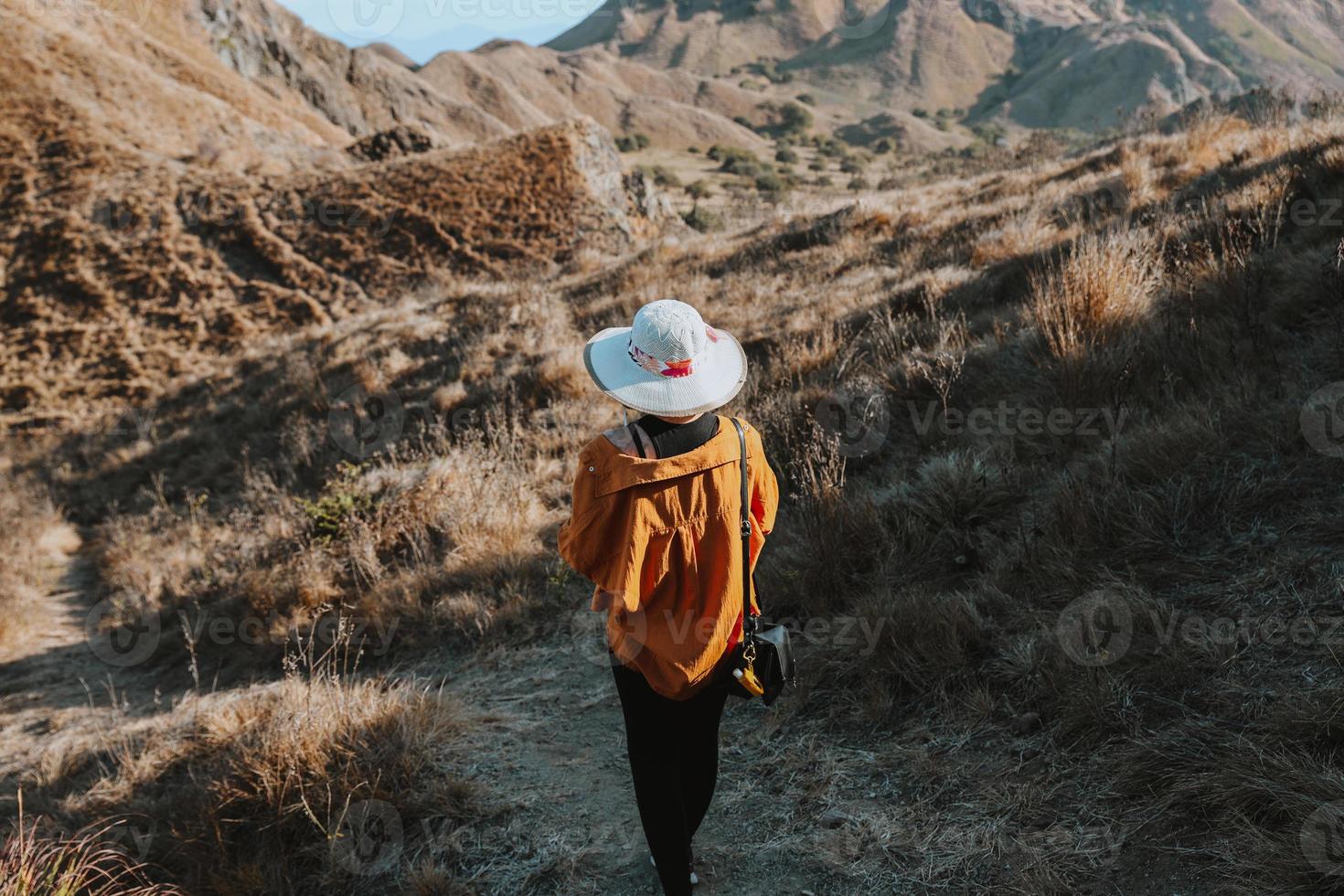 weibliche touristin mit sommerhut, die allein auf der insel padar den hügel hinuntergeht foto