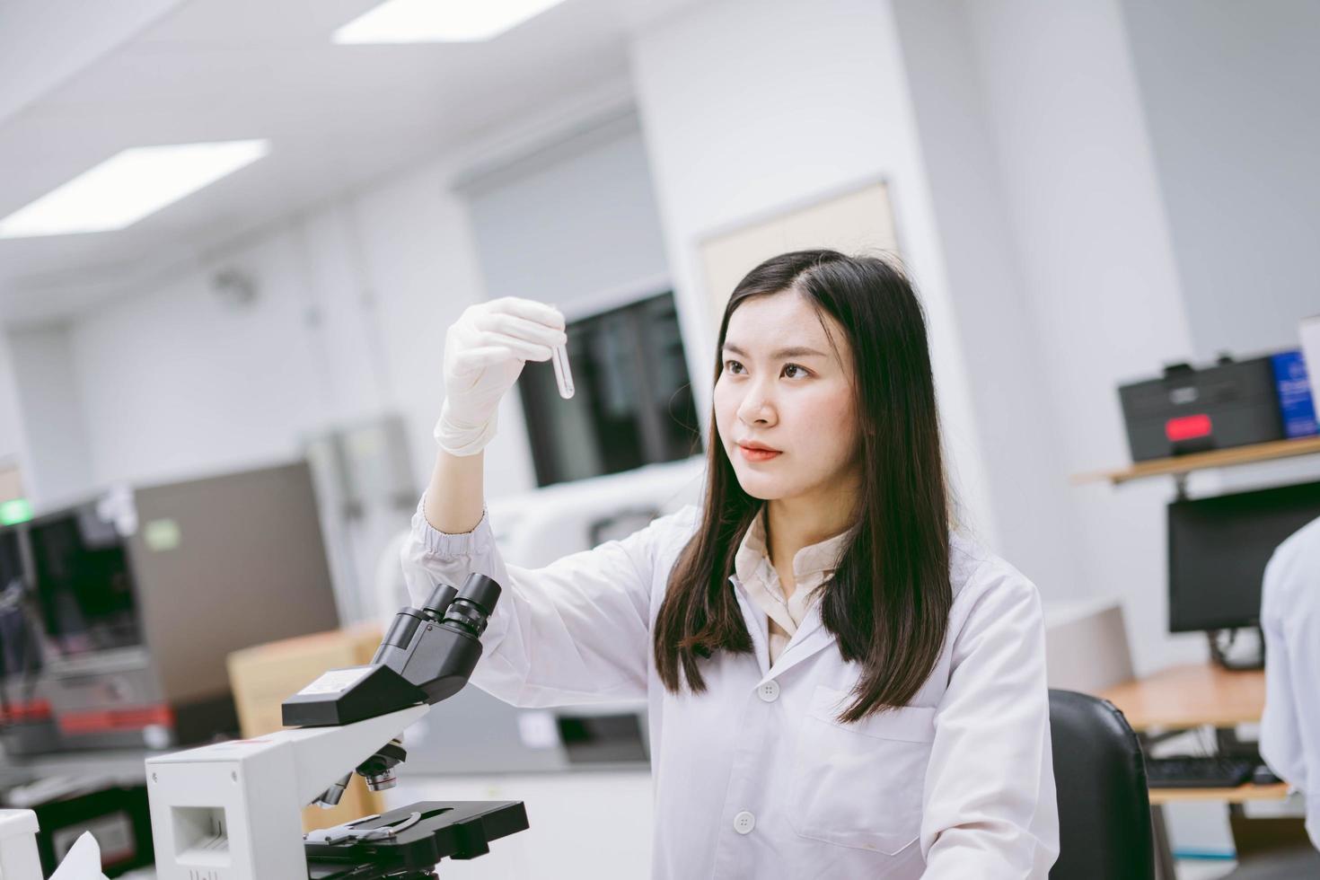 junge medizinische wissenschaftlerin, die reagenzglas im medizinischen labor betrachtet foto