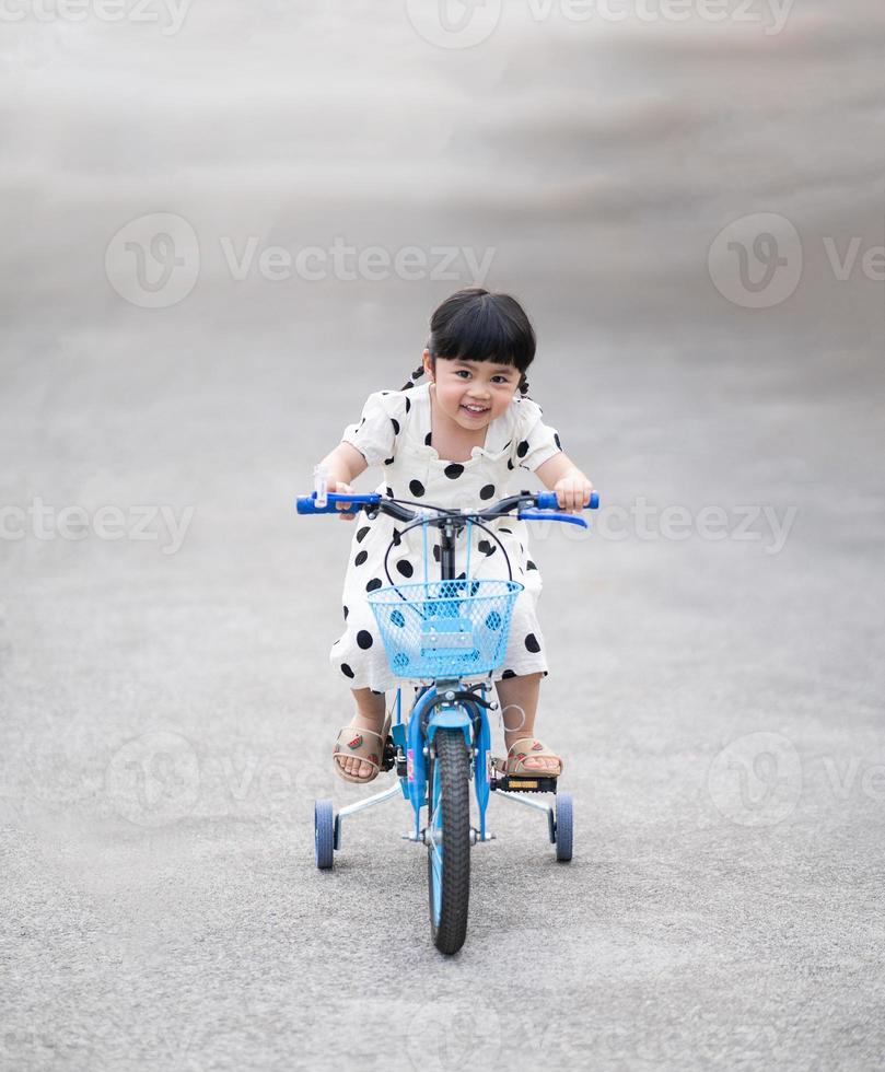 asiatisches babymädchen lächelnd glücklich, fahrrad auf der straße zu fahren, kinderradfahren auf der straße, babysportaktivitätskonzept foto