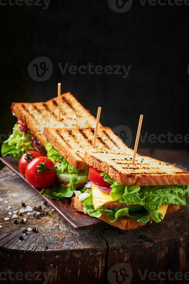 hausgemachtes Sandwich mit Schinken, Salat, Käse und Tomaten auf Holzhintergrund foto