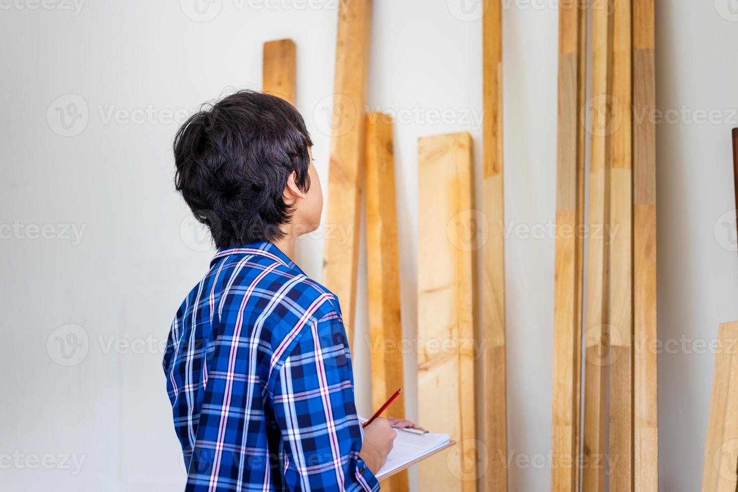Junger Tischler, der den Holzvorrat im Werkslager überprüft. Mann zählt Holzbalken Holzinventar in der Tischlerei foto