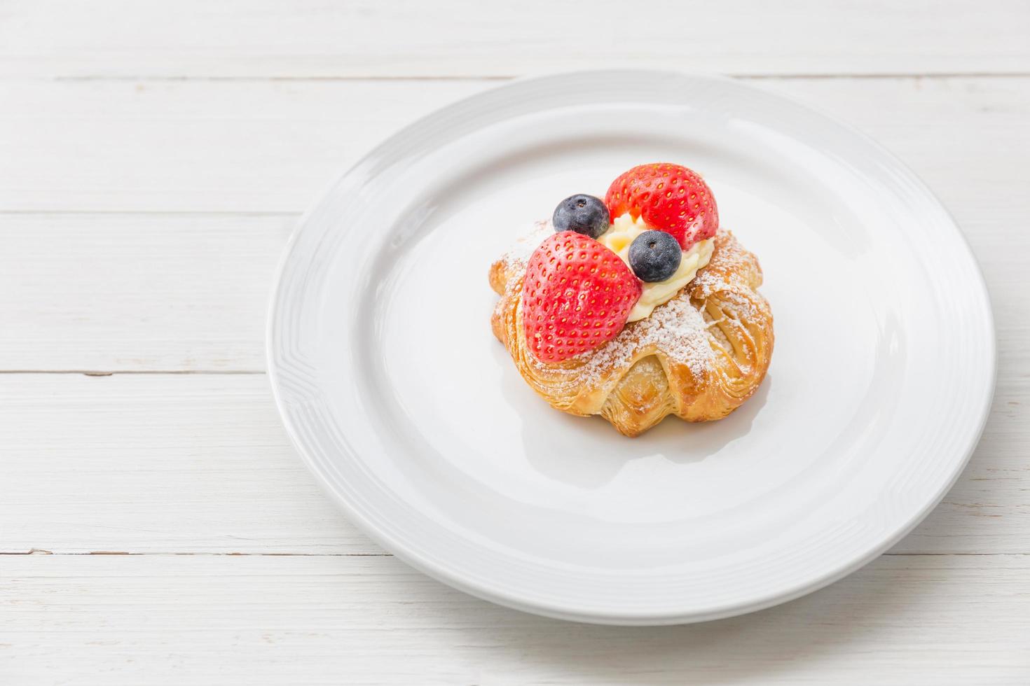 Frisches Croissant mit Schlagsahne und Erdbeeren Heidelbeeren auf einem weißen Teller foto