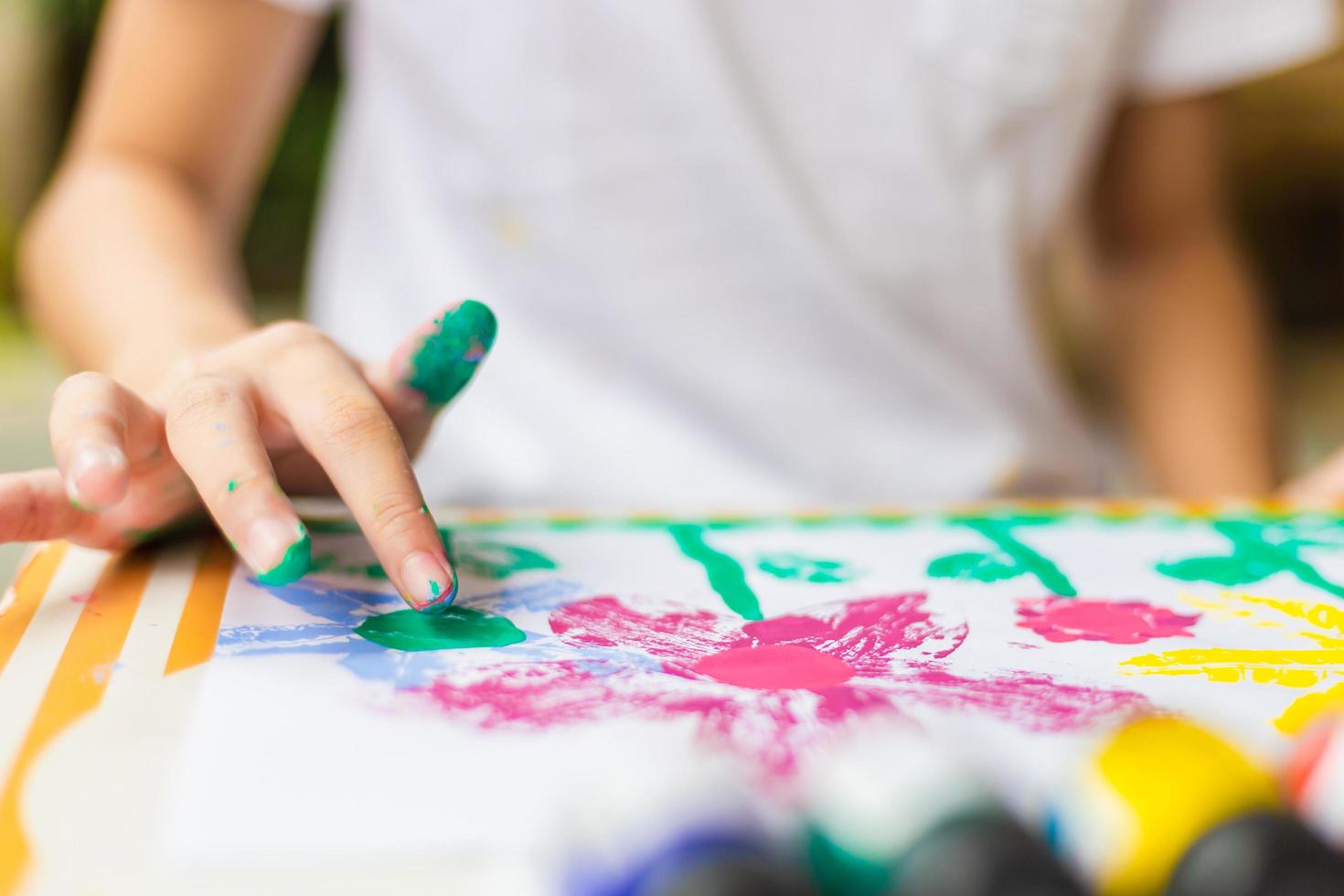 Kind am Tisch zeichnet mit Wasserfarbe, fröhliches kleines süßes Mädchen spielt und lernt mit dem Färben der Farben foto