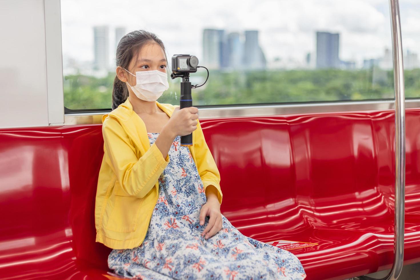 mädchen mit action-kamera, kind tragen gesichtsmaske während des ausbruchs von coronavirus und grippe, reisen mit der bahn. foto