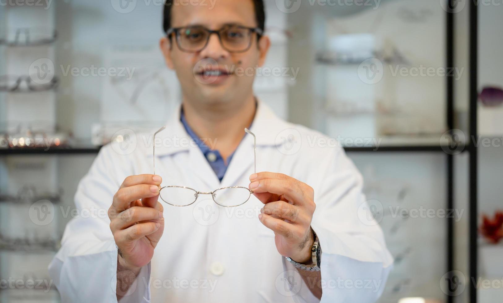 Fröhlicher Optometrist-Mann mit Brille im Optikgeschäft, glücklicher Inder, der eine Brille im Optikgeschäft auswählt foto