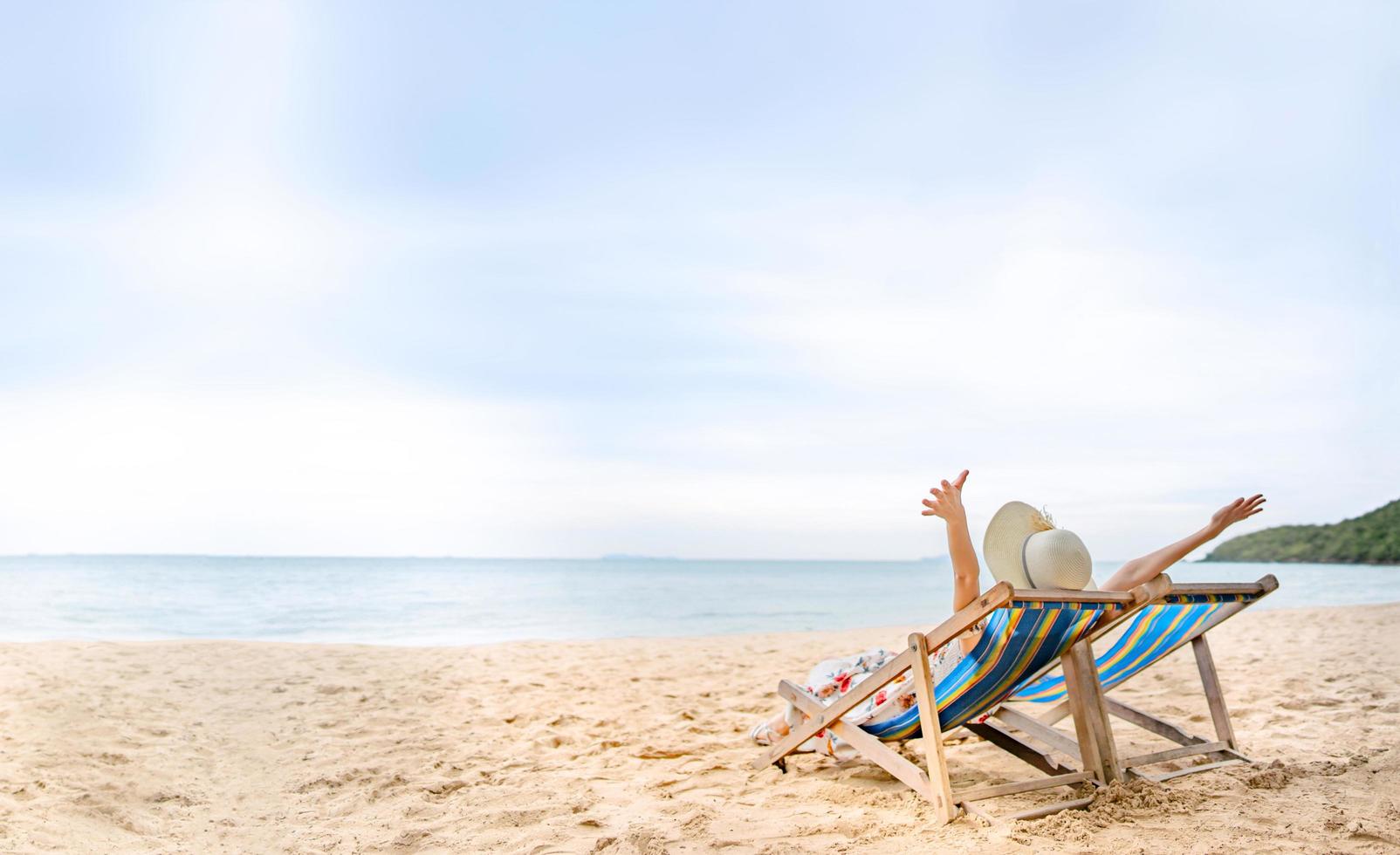 junge asiatische frau, die sich auf strandstuhl entspannt, bewaffnen sie ihre hand mit schlapphut foto