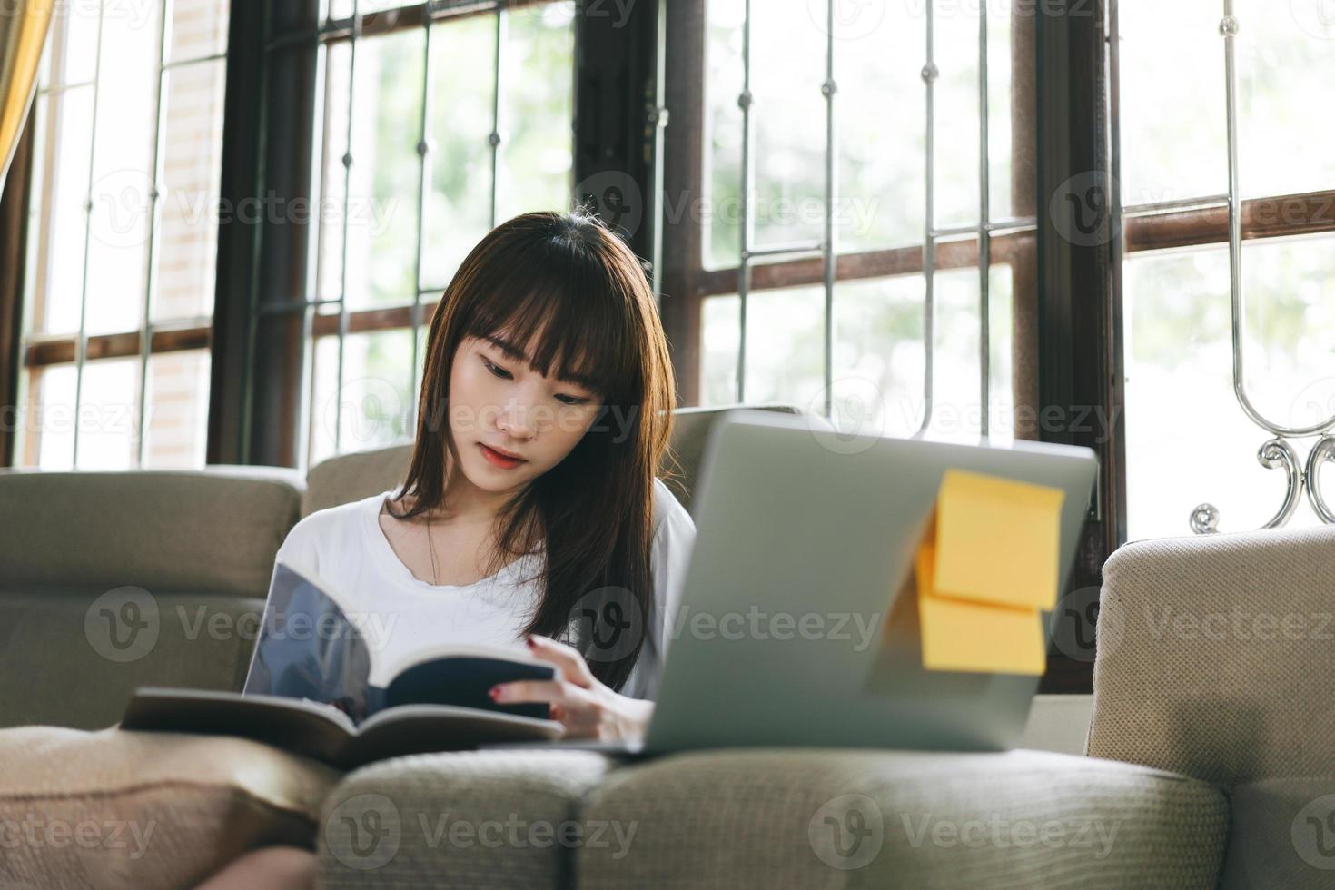 asiatische jugendlicherfrau, die buch mit laptop lernt und liest. foto