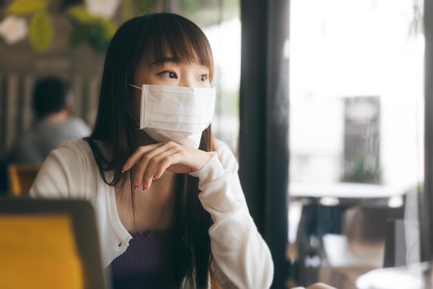 junge erwachsene asiatische frau mit schützender gesichtsmaske für virus covid 19 arbeiten und lernen am tag im café. foto