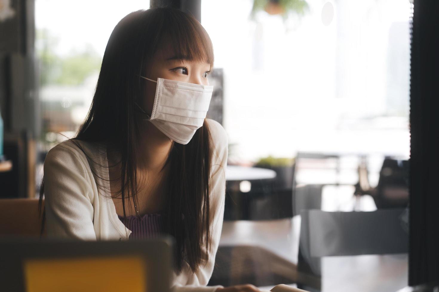 junge erwachsene asiatische studentin mit gesichtsmaske für viruskorona oder covid 19 studie im café. foto