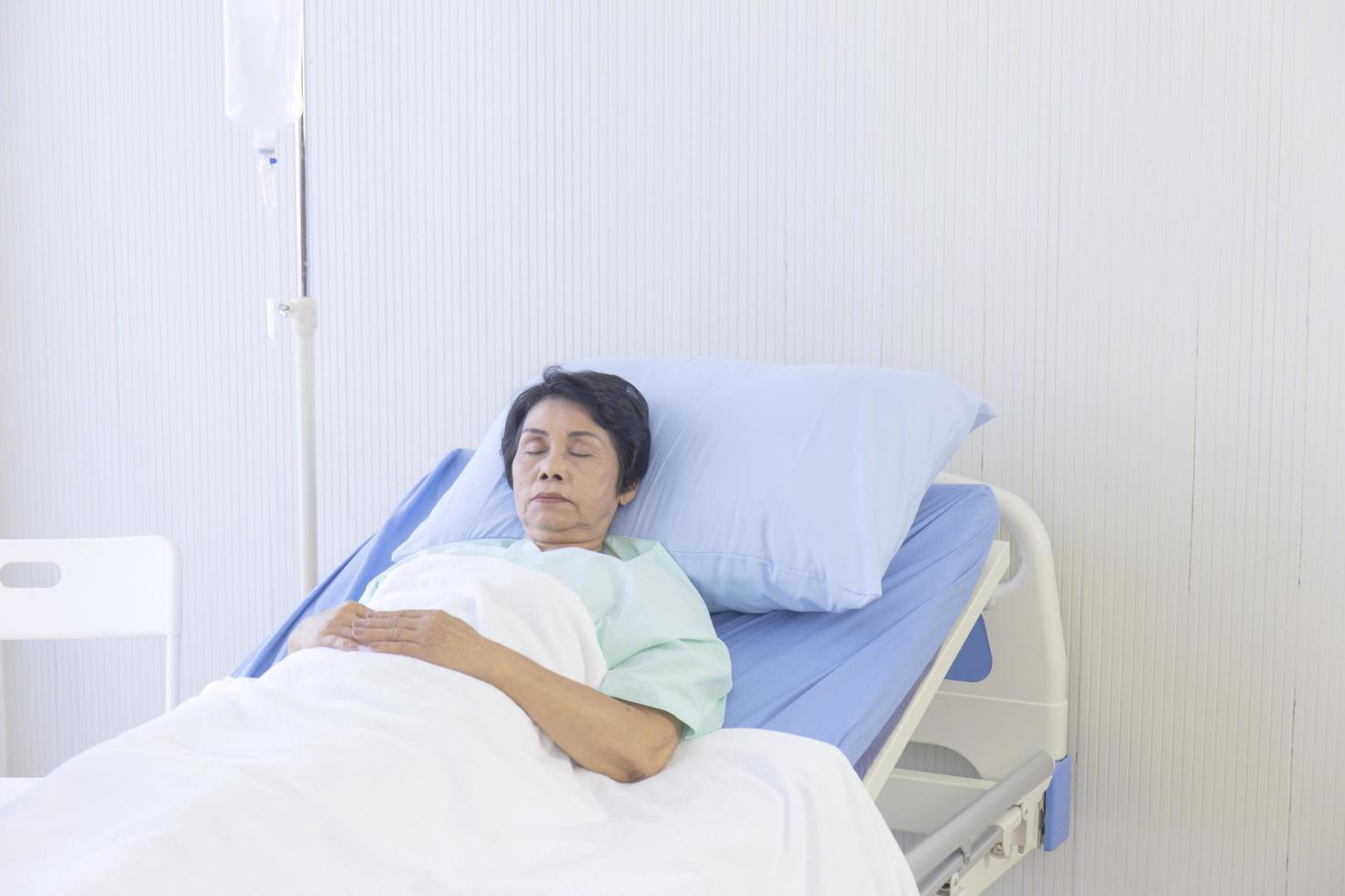 Die älteren asiatischen Frauen schlafen in einem Krankenhausbett. foto