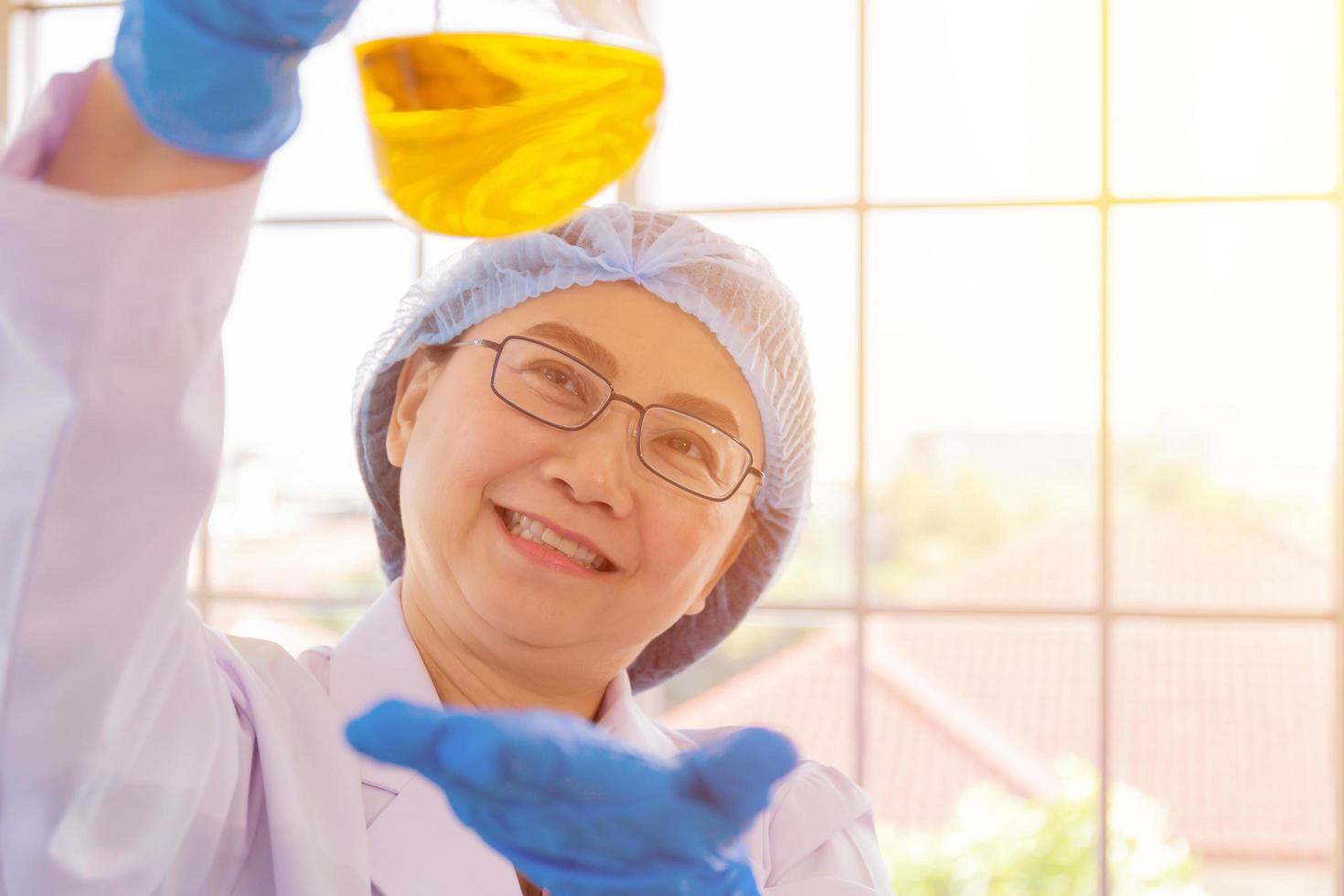 ein heilmittel entdecken für eine asiatische wissenschaftlerin, die konzentriert ein reagenzglas in der hand hält und beim arbeiten zuschaut. foto