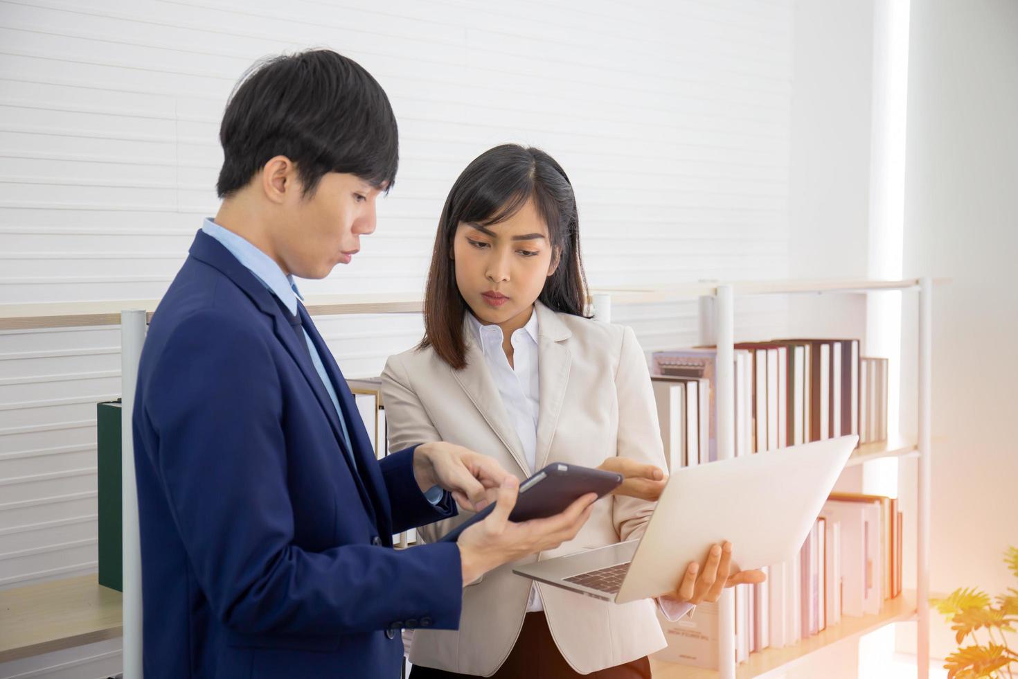 Zwei junge asiatische Geschäftsleute treffen sich im Büro in der Hand des Tablets. foto