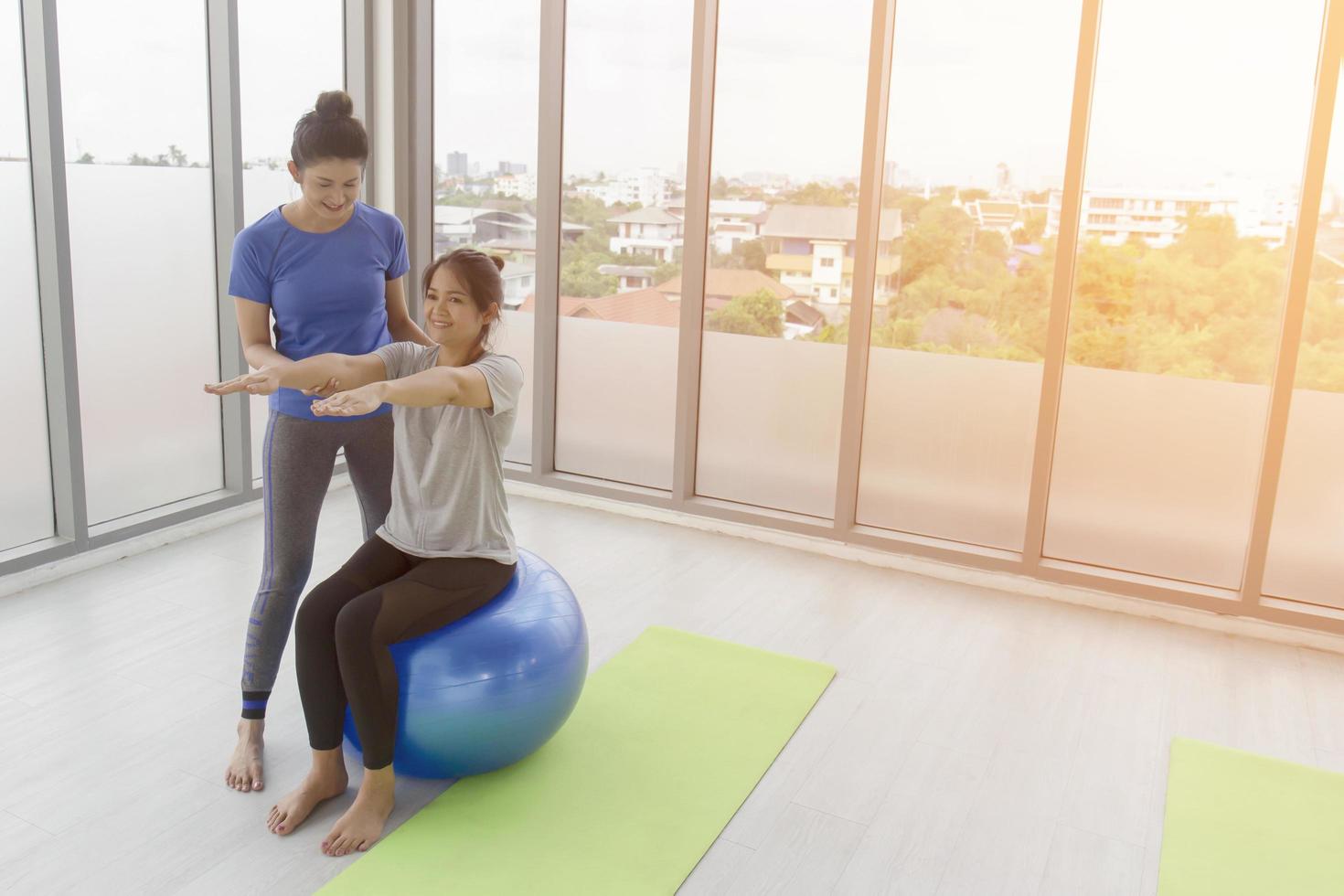 Eine Trainerin bringt einer asiatischen Kundin mittleren Alters Yoga bei, während sie auf einem Gummiball in einer Turnhalle sitzt. foto