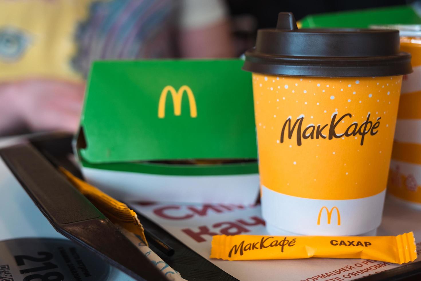 ein pappbecher mcdonald's kaffee mit der aufschrift maccafe auf russisch und ein hamburger in einer schachtel auf einem tablett. Fast-Food-Restaurantketten. Russland, Kaluga, 21. März 2022. foto