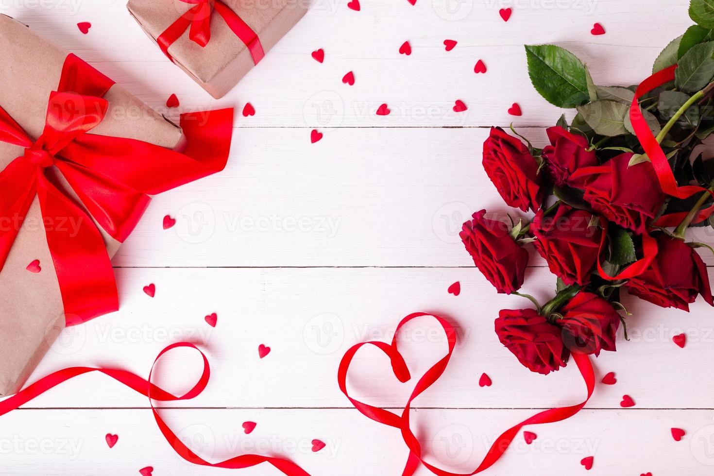 rotes band in herzform, rosenstrauß, herzen und geschenkboxen in kraftpapier auf weißem holztisch. foto