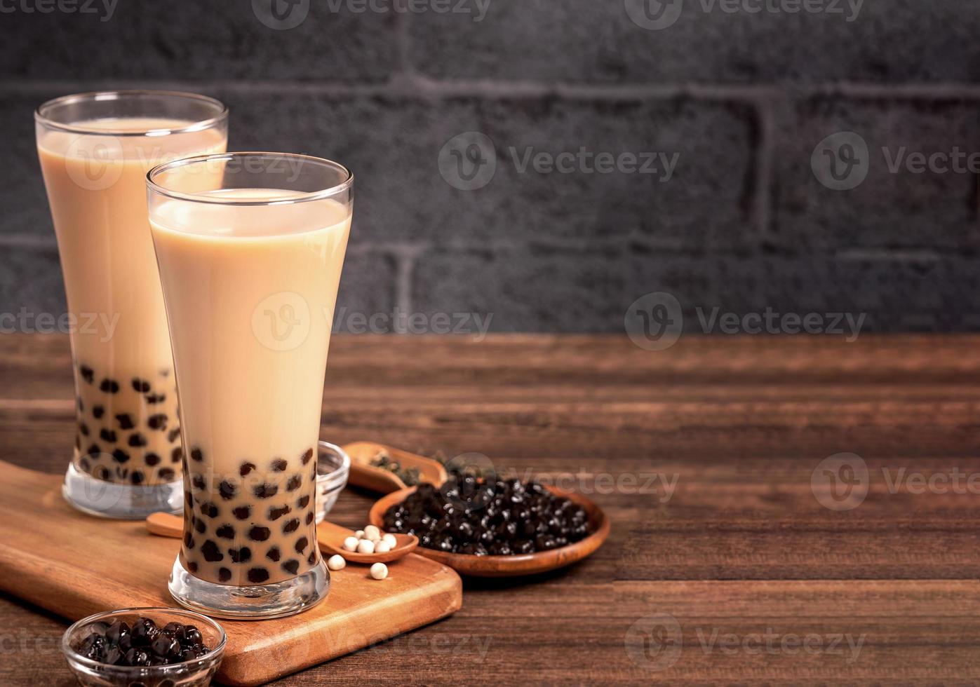 Köstlicher Blasenmilchtee mit Tapioka-Perlenkugel im Glas auf Holztisch und dunkelgrauem Backsteinhintergrund, beliebte Speisen und Getränke in Taiwan, Nahaufnahme foto